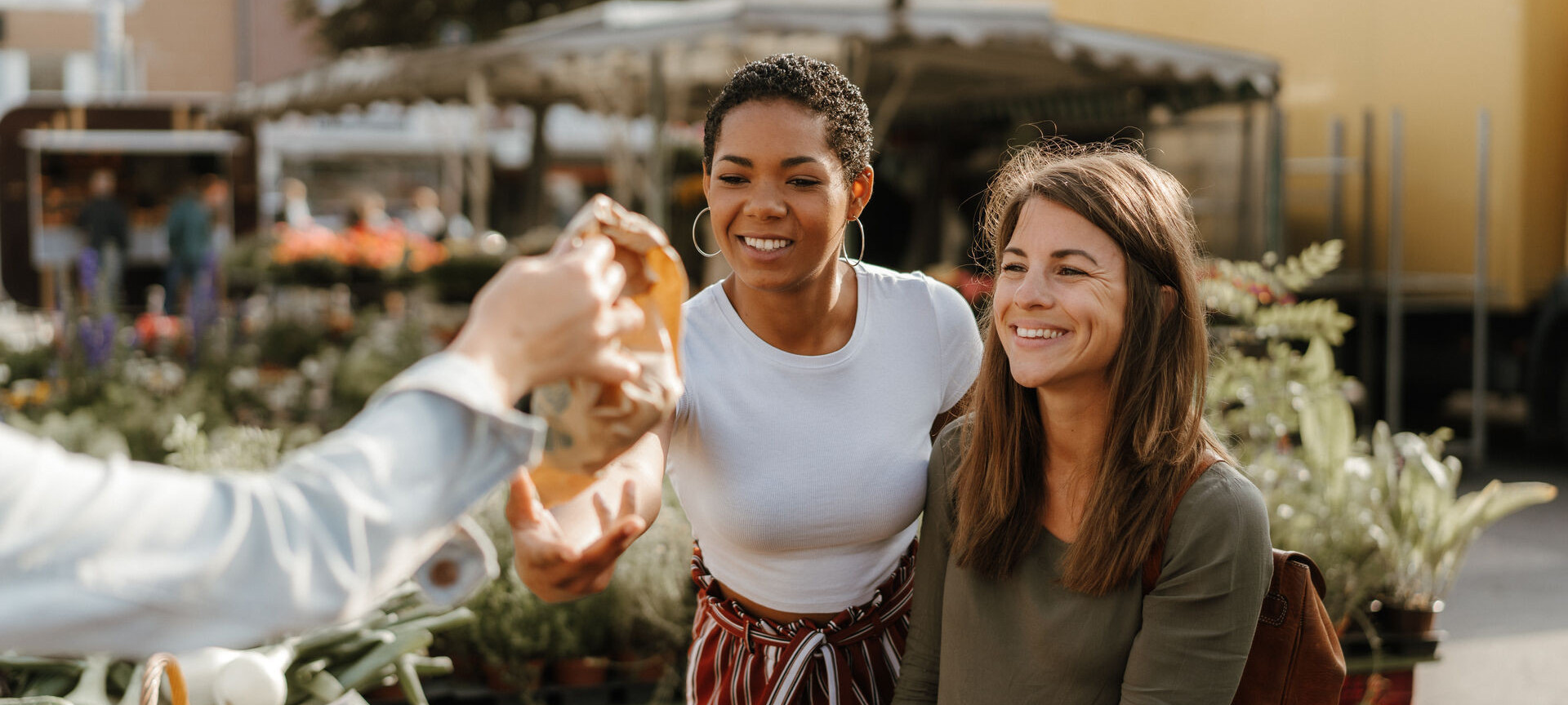 Zwei Frauen sind auf dem Wochenmarkt und bekommen eine Tüte überreicht