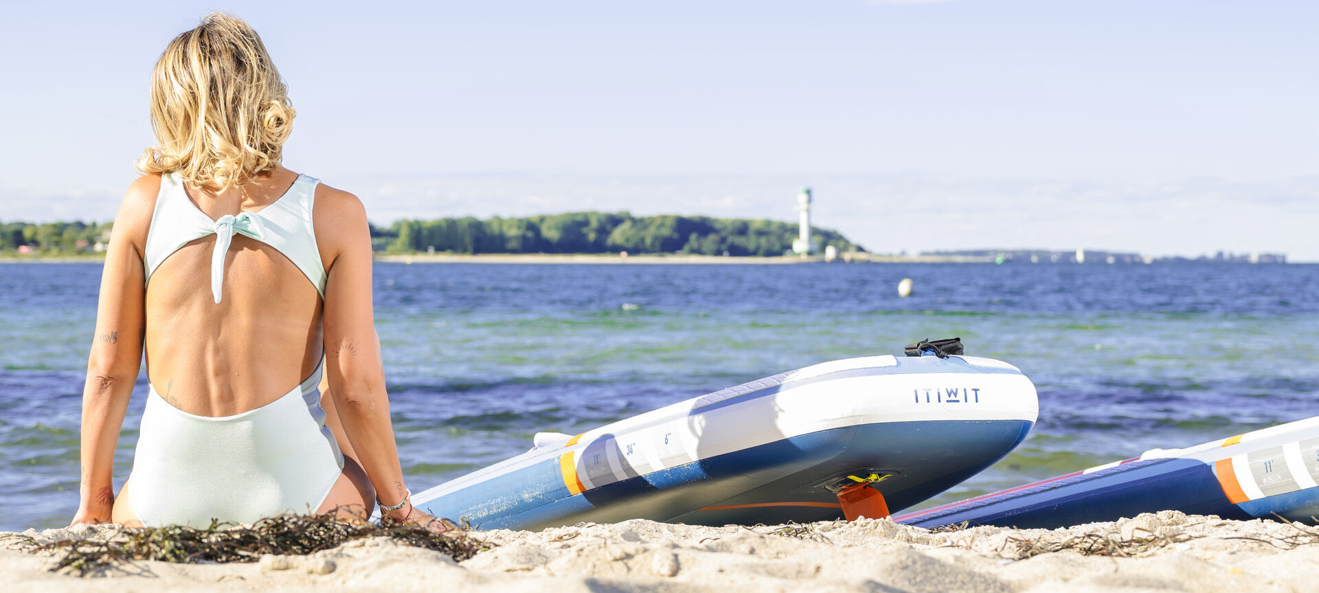 Frau sitzt mit SUP am Strand und schaut auf das Meer