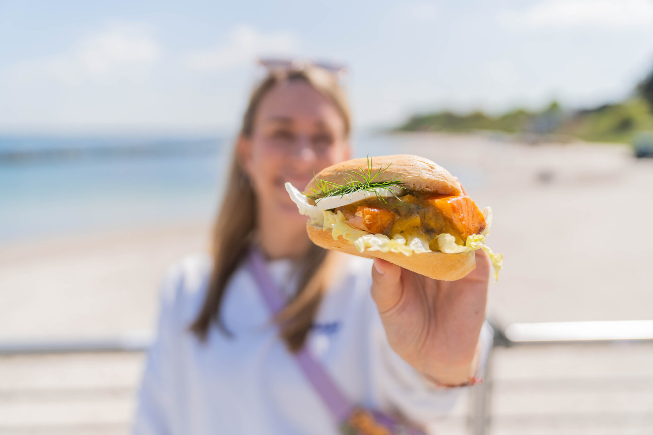 Eine Frau hält ein Fischbrötchen in die Kamera