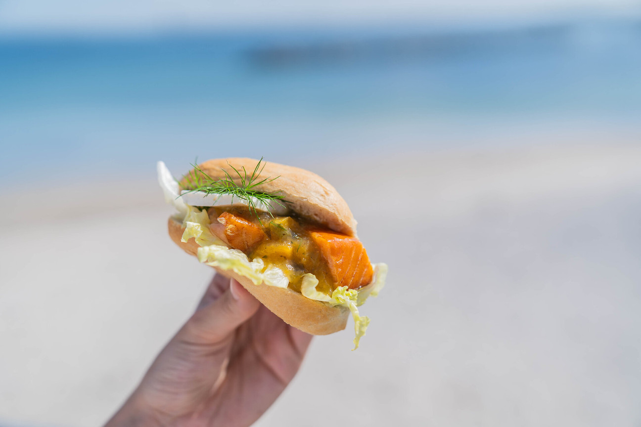 Hand hält Fischbrötchen mit Meer im Hintergrund