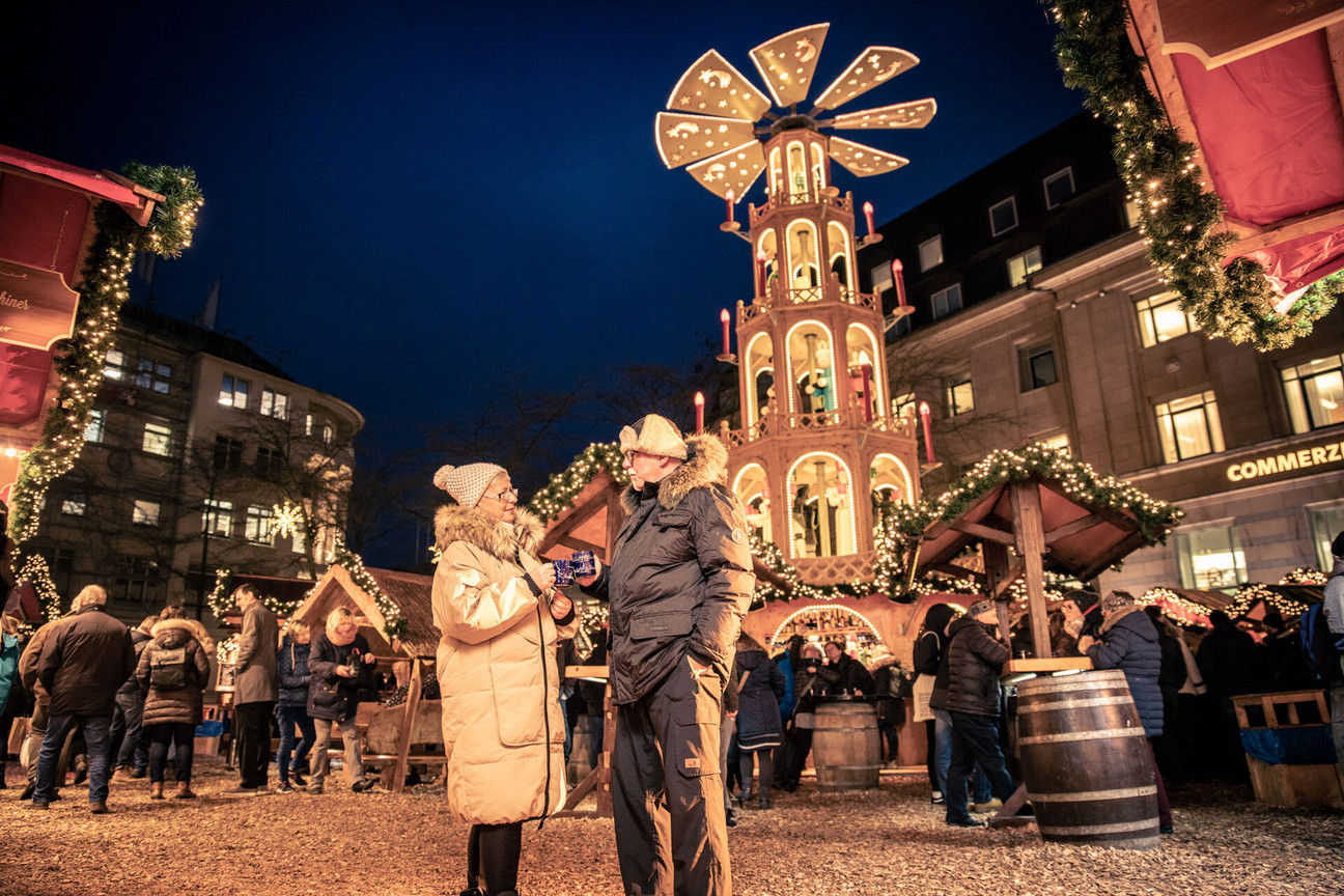 Ein Paar steht mit jeweils einer Tasse Punsch in der Hand auf dem Weihnachtsmarkt vor einer großen Leuchtpyramide