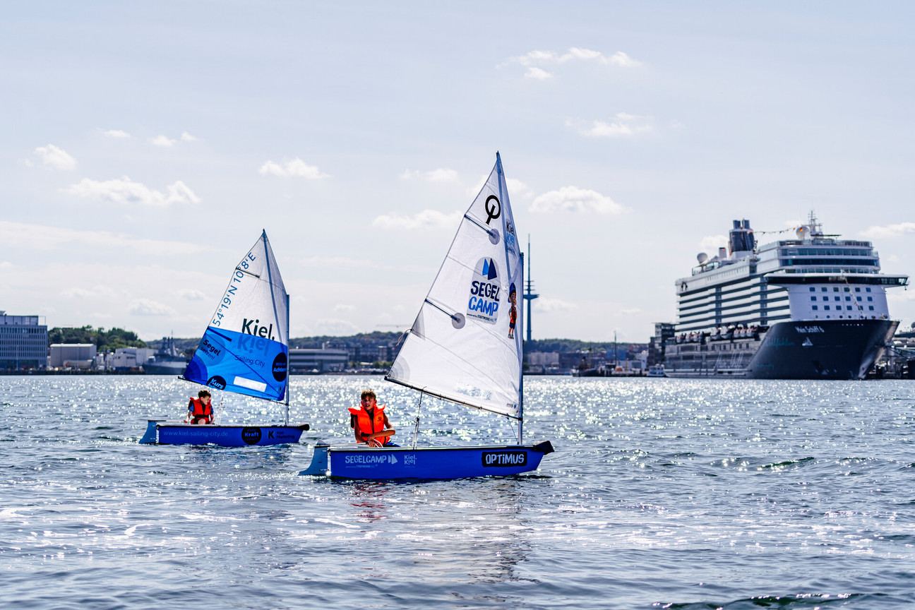 Zwei Optimisten auf der Kieler Förde, Kreuzfahrtschiff im Hintergrund