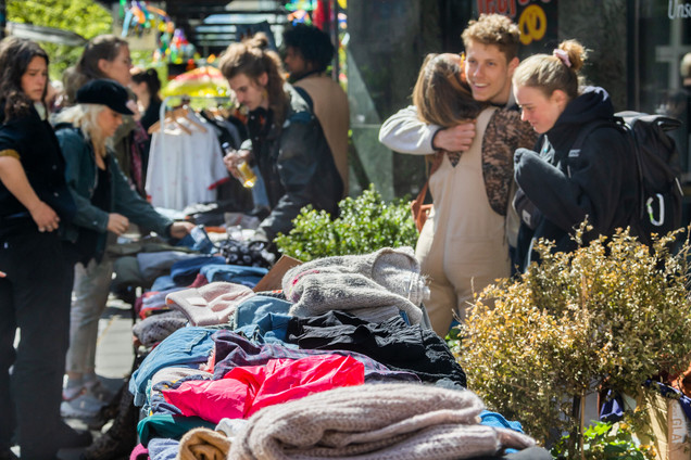 Viele Kleidungsstück auf dem Tisch auf dem Flohmarkt und viele Menschen im Hintergrund