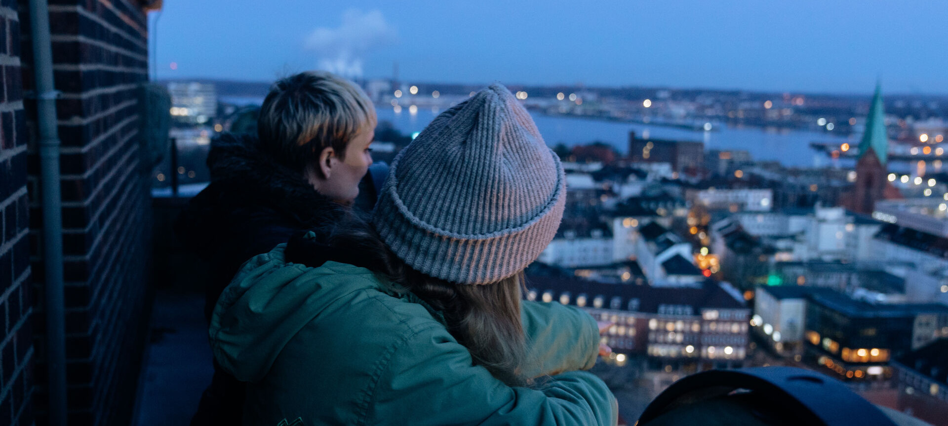 Zwei Gäste genießen den Ausblick über Kiel vom Rathausturm aus am Spätnachmittag im Winter