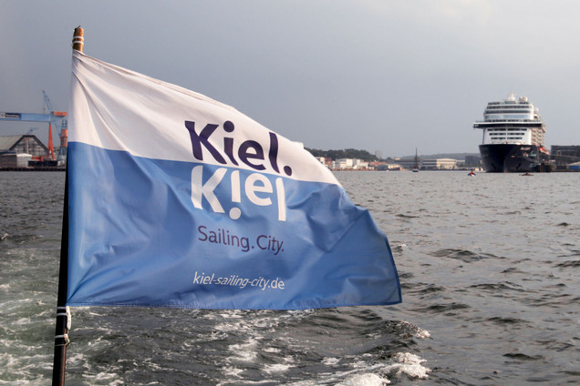 Flagge mit dem Logo der Stadt Kiel und im Hintergrund die Förde