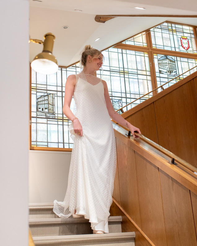 Frau modelt in langem festlichen weißem Kleid mir dünnen Trägern im schönen hellen Treppenaus