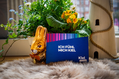 Geschenktipp für OStern: Kielgutschein mit der Aufschrift "Ich fühl mich Kiel" neben Schokohasen und Blumen plaziert