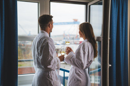 Pärchen im Hotelzimmer mit Blick auf die Förde und Sektglas in der Hand