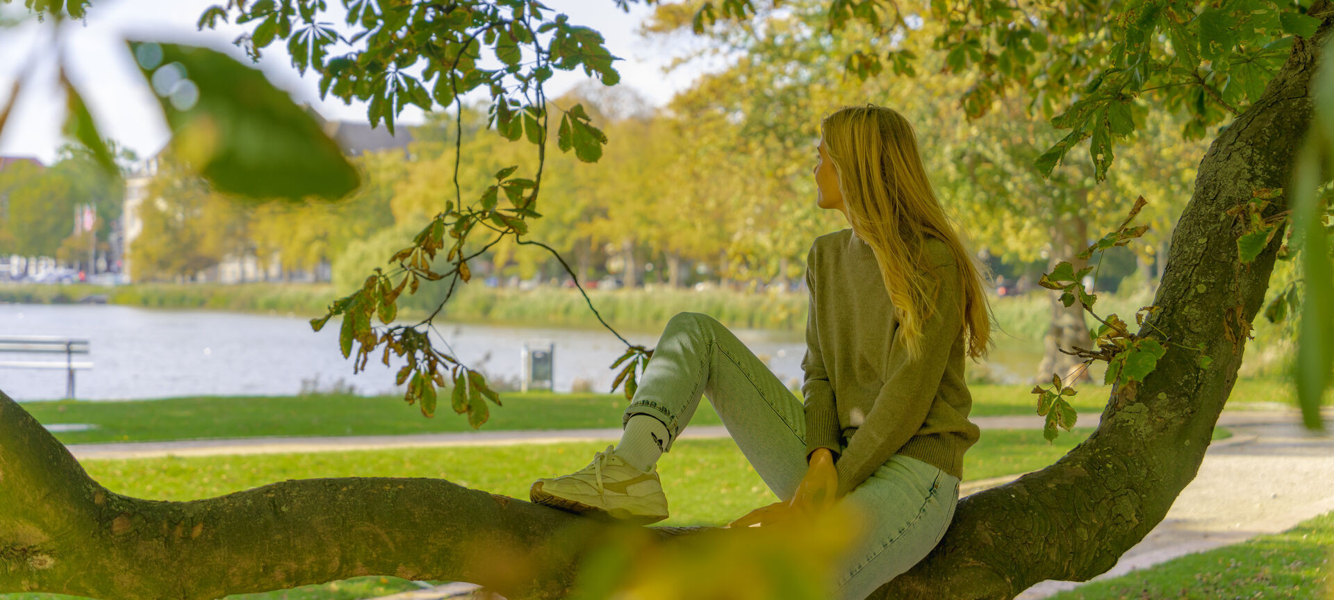 Frau sitzt auf Baumstamm und schaut auf den kleinen Kiel im Herbst