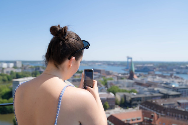 Frau steht auf dem Rathausturm und macht ein Foto von der Skyline