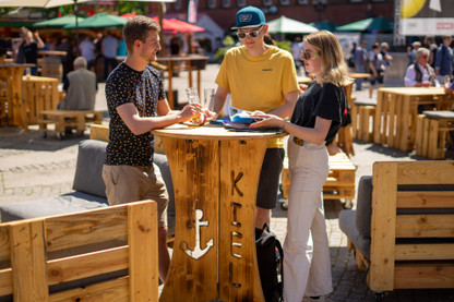 Zwei Männer und eine Frau essen auf dem internationalen Markt zur Kieler Woche