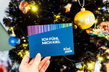 KielGutschein mit geschmücktem Weihnachtsbaum im Hintergrund
