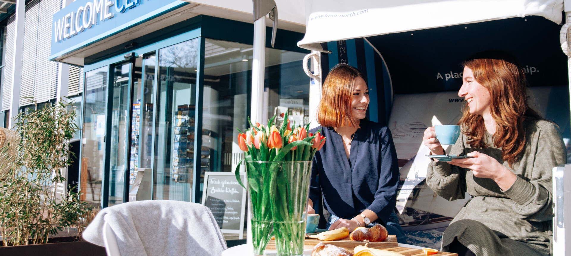 Zwei Frauen sitzen in einem Strandkorb vor dem Welcome Café und trinken Kaffee zusammen