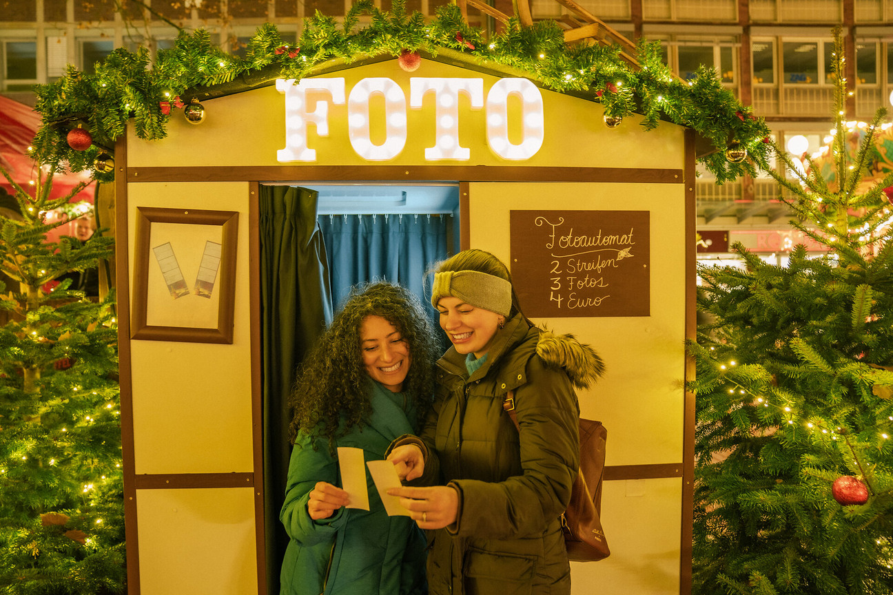 Zwei Frauen schauen ihre Fotos vor einer weihnachtlich geschmückten Fotobox an